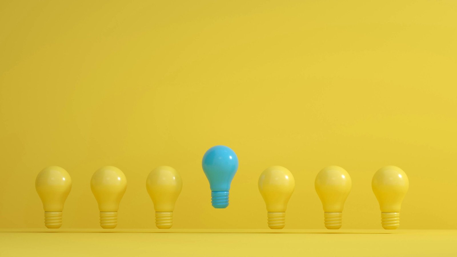 A standout blue light bulb among several yellow bulbs on a yellow background, symbolizing innovation.